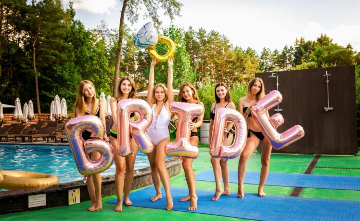 women holding balloons spelling out bride by the swimming pool