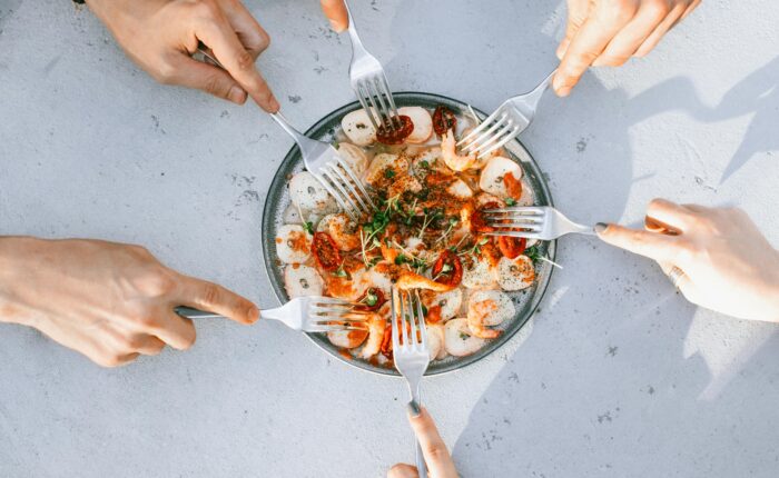 a plate of seafood with multiple hands putting their forks in it