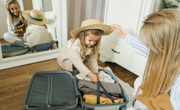 a girl in a hat putting clothes in a suitcase