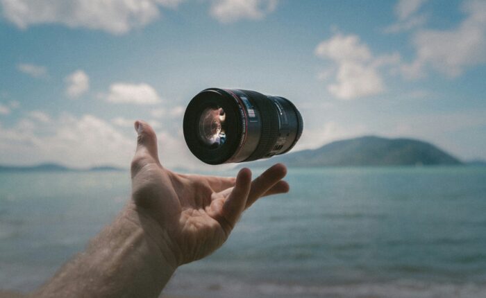 a camera lens floating above a hand against a beach backdrop